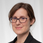 A headshot of Dr. Mika Ahuvia against a gray background