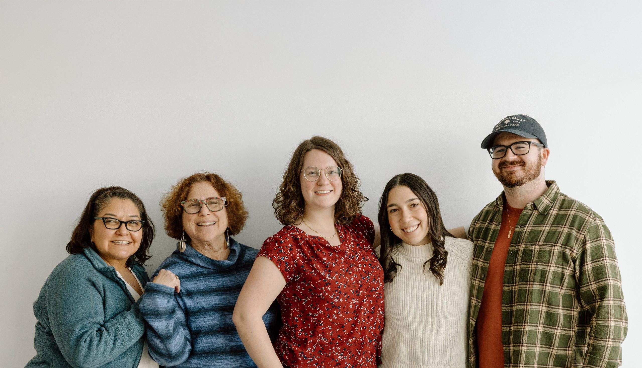 8 adults stand in a line smiling. Many have arms raised in celebration.